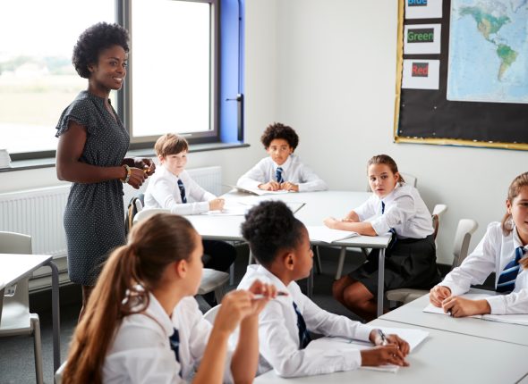 Female,High,School,Tutor,Helping,Students,Wearing,Uniform,Seated,Around